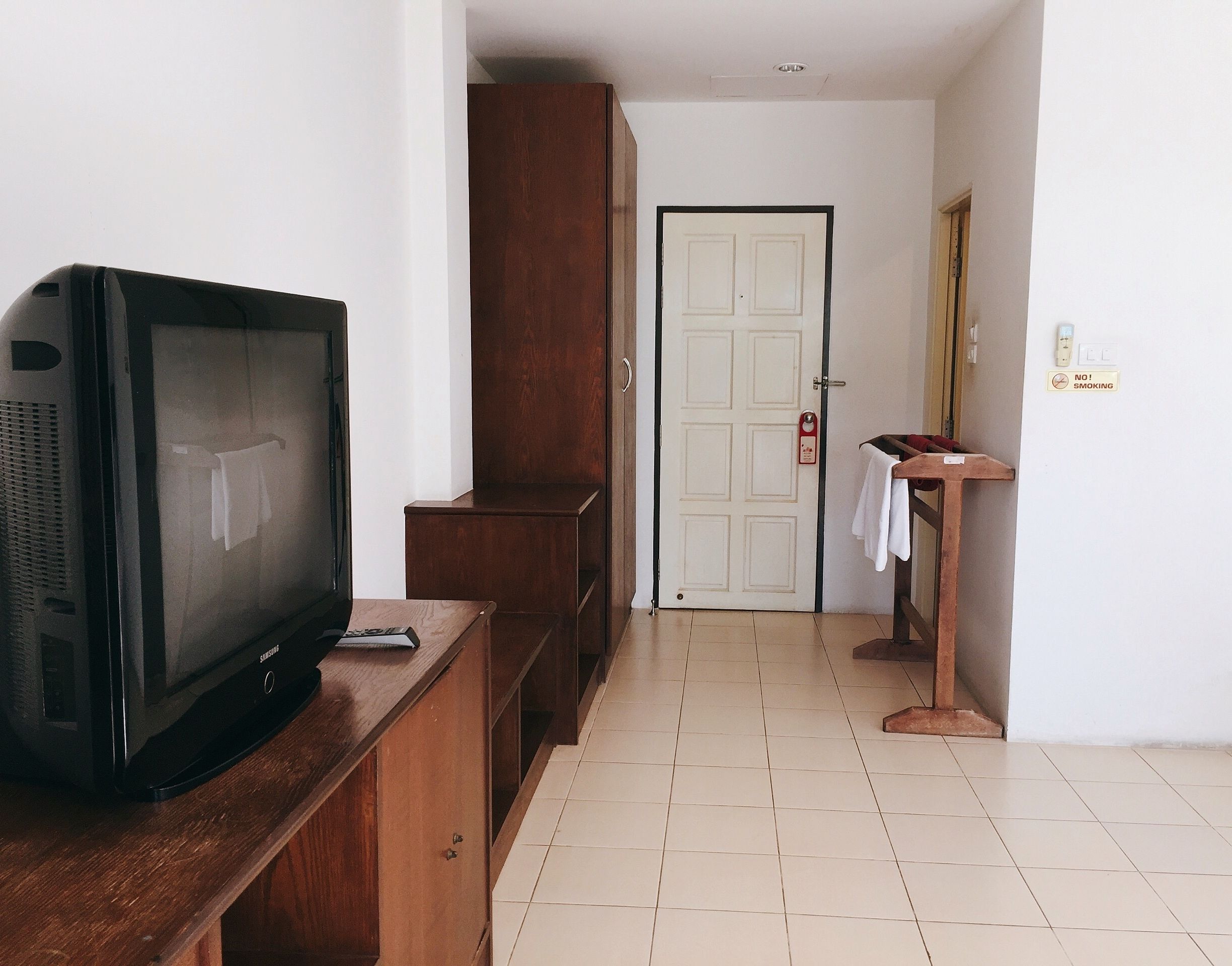 A room with a television on a wooden stand, a door with a red handle, and a small table with a towel on it.