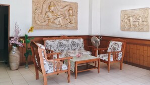 A room with a wooden sofa set, a ceiling fan, and two wall-mounted decorative carvings. - Rawai Guesthouse (Chalong)