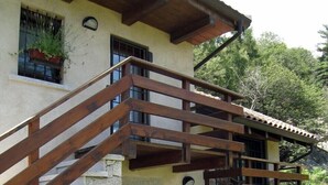 Un edificio a due piani con facciata in pietra, ringhiere del balcone in legno e una panchina in pietra all'esterno.