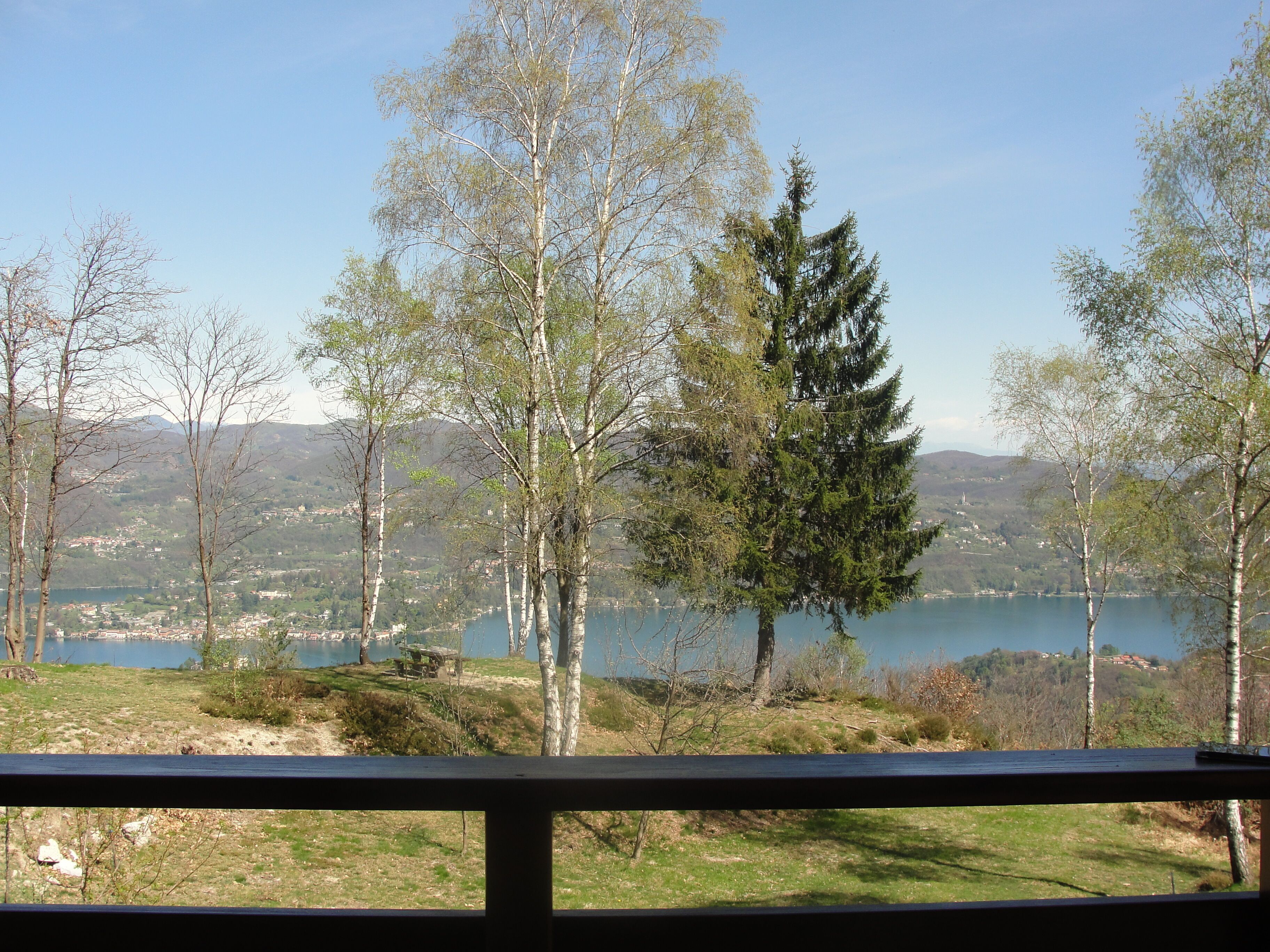 A view from a balcony overlooking a lake with trees and distant buildings.
