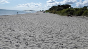 Ein Sandstrand mit Fußspuren, ein klarer Himmel und Bäume in der Ferne.