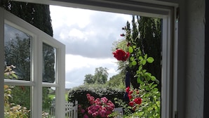 Eine weiße Tür führt in einen Garten mit Kiesweg, rosa und roten Blumen und einem weißen Zierzaun.