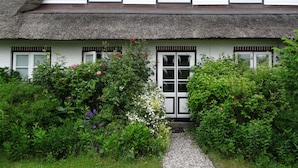 Ein traditionelles Haus mit einem Strohdach, weißen Wänden und einem Kiesweg, der zum Eingang führt.