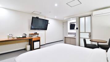 A hotel room with a bed, a desk with a flat-screen TV, a small kitchenette, and a seating area with a table and chairs.