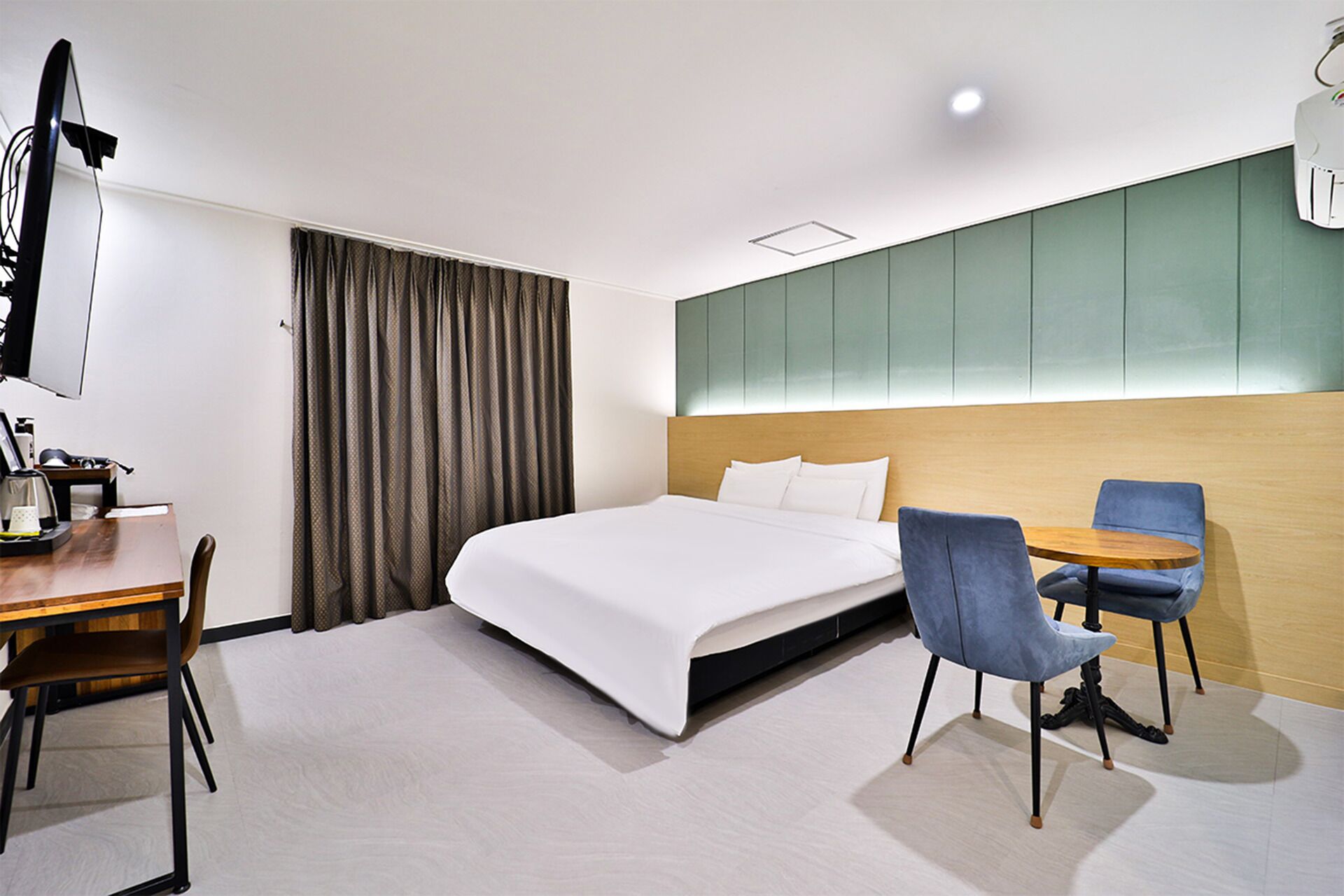 A hotel room with a bed, a desk with a chair, a small round table with a chair, and a television.