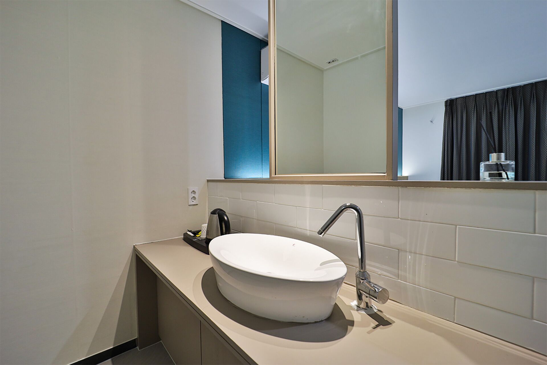 A modern bathroom with a large oval sink, a mirror above the sink, and a dark curtain in the background.