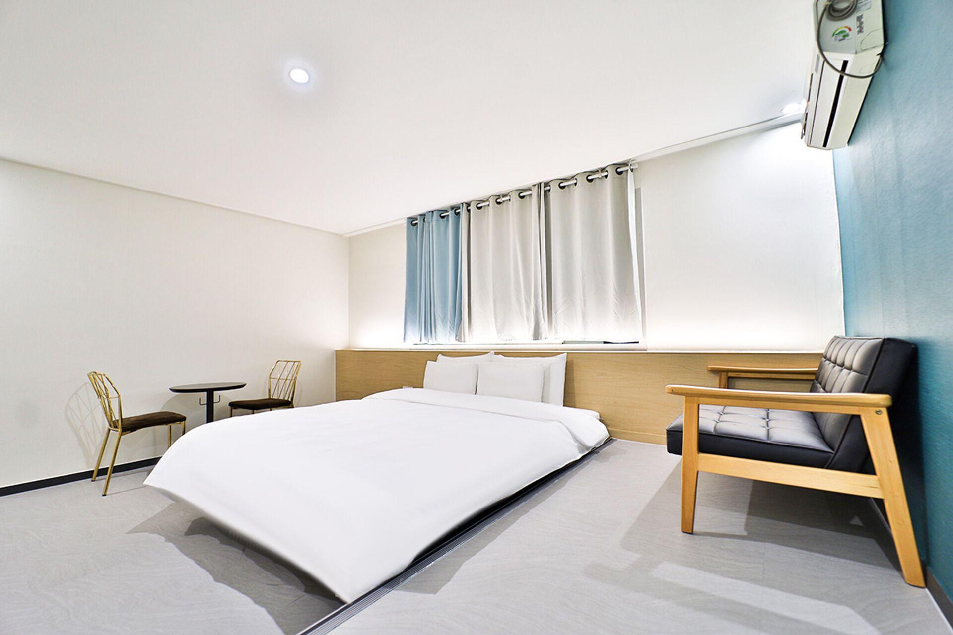 Habitación de hotel moderna con una cama grande, un escritorio, una silla y un ventanal con cortinas.