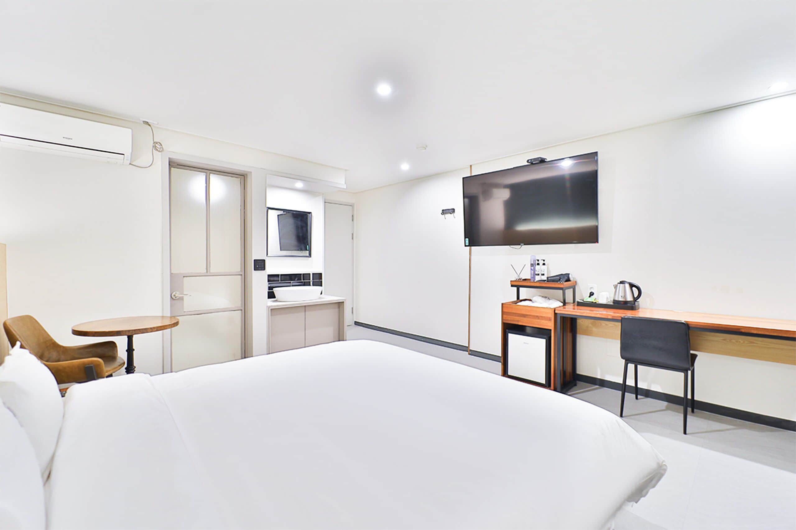 Ein Hotelzimmer mit Bett, Schreibtisch, Stuhl, Fernseher und einer kleinen Küchenzeile.
