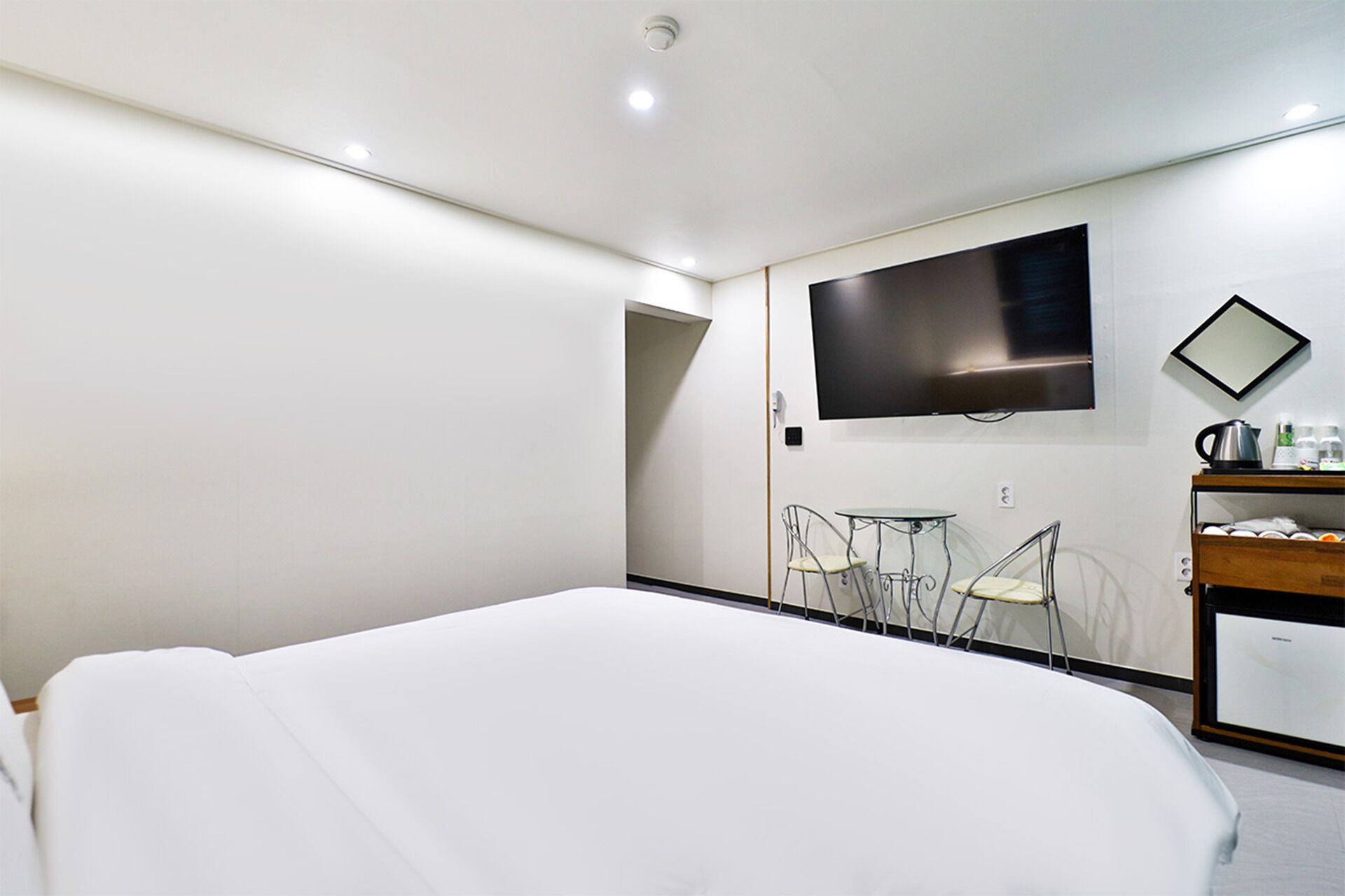 Quarto de hotel moderno com uma cama grande, televisão de tela plana na parede, uma pequena mesa com cadeiras e um minibar.