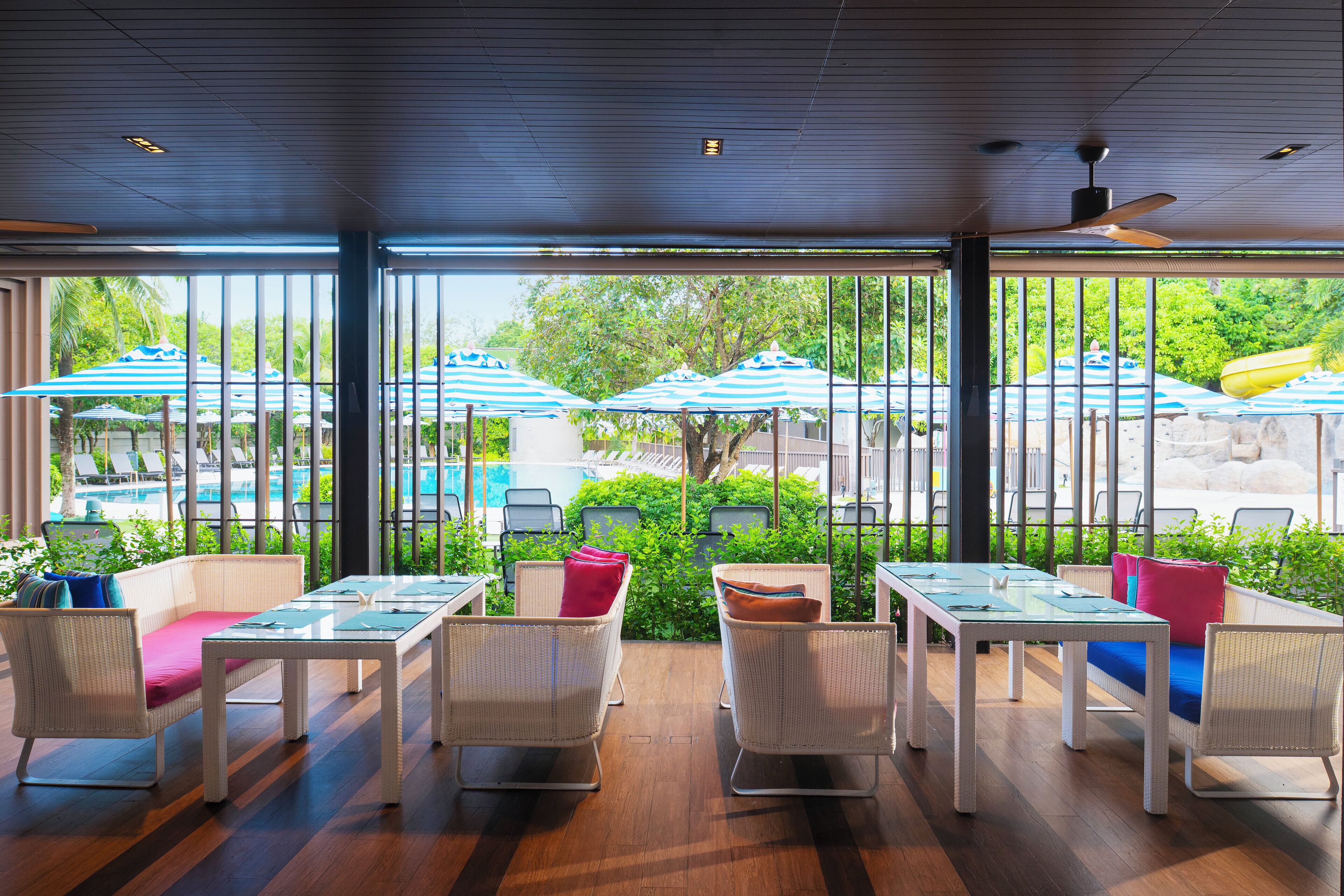 Un restaurante con terraza, mobiliario de mimbre blanco y sombrillas a rayas azules.