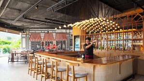 Uma área de bar com banquetas de madeira, um balcão e um bartender.