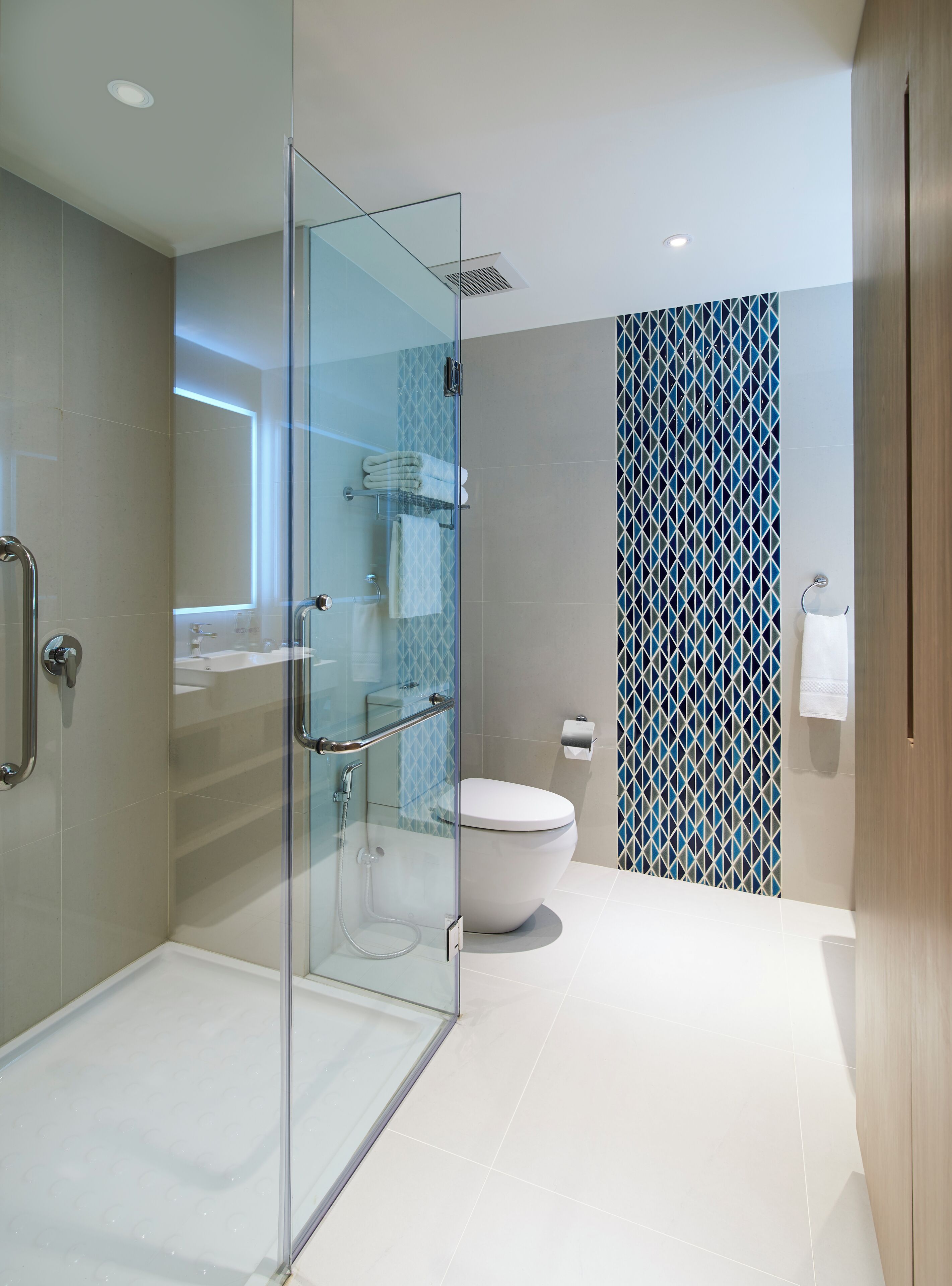 A modern bathroom with a glass shower enclosure, a white toilet, and a patterned wall.