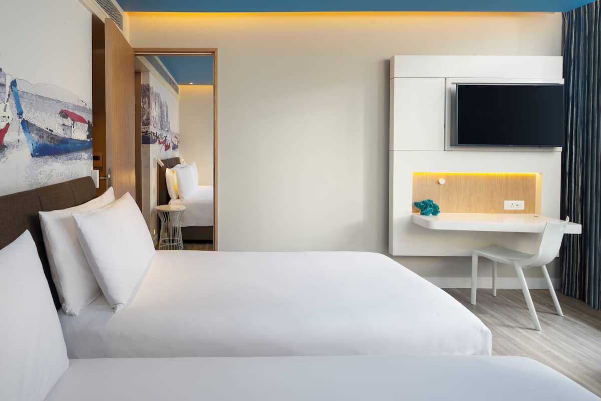 A modern hotel room with a large bed, a desk with a chair, a flat-screen TV, and a painting on the wall.