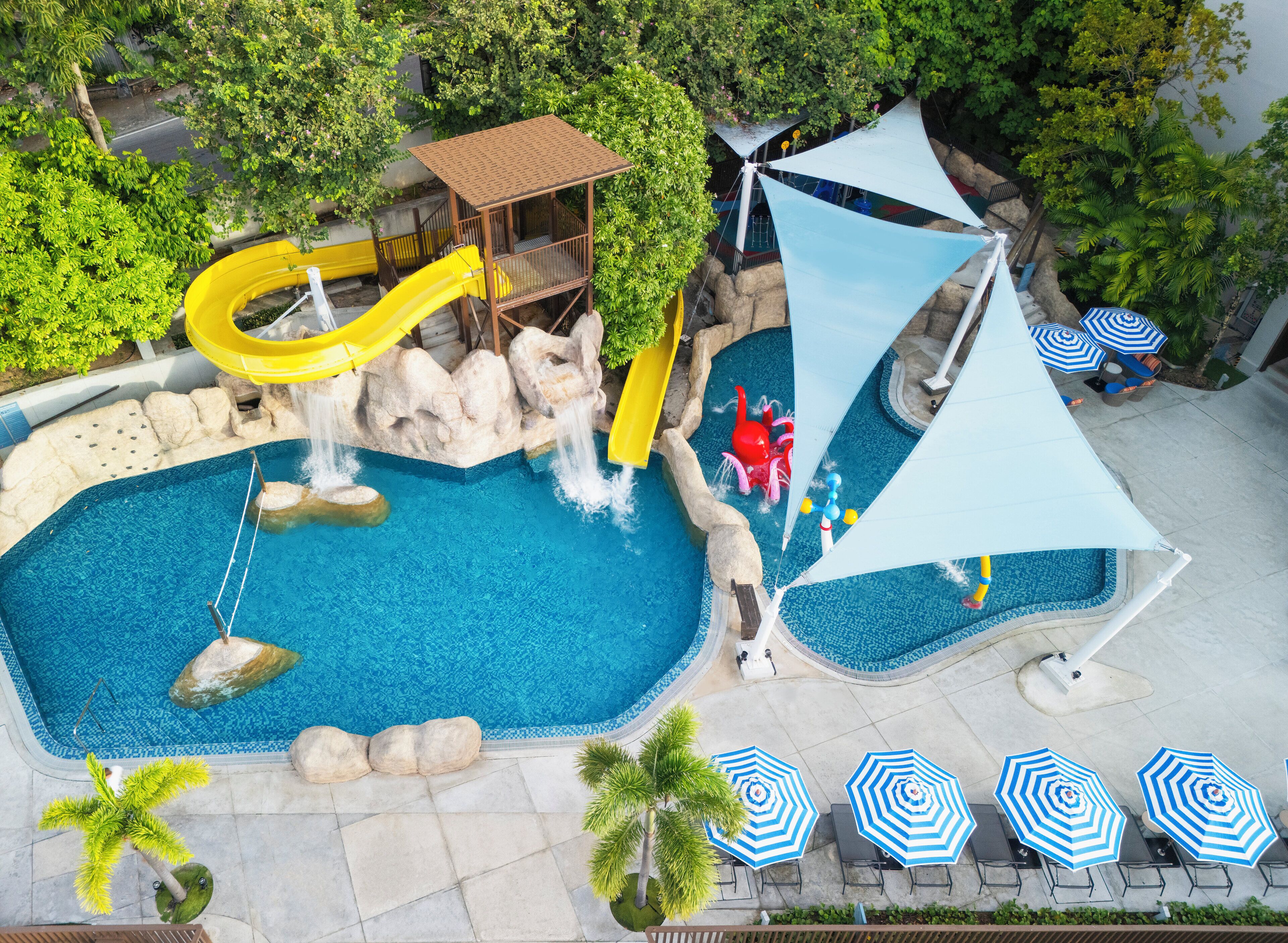 Una piscina con tobogán, zona de juegos y sombrillas.