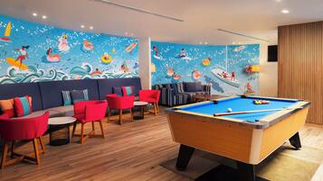 A pool table in a room with a mural of swimmers and boats, red and blue seating, and wooden flooring.