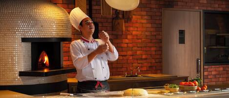 A chef in a kitchen with a brick wall, a wood-fired oven, and a counter with ingredients and utensils.