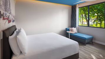 Ein modernes Hotelzimmer mit einem großen Bett, einer kleinen Sitzecke, einem Deckenventilator und einem großen Fenster mit Blick auf Bäume.