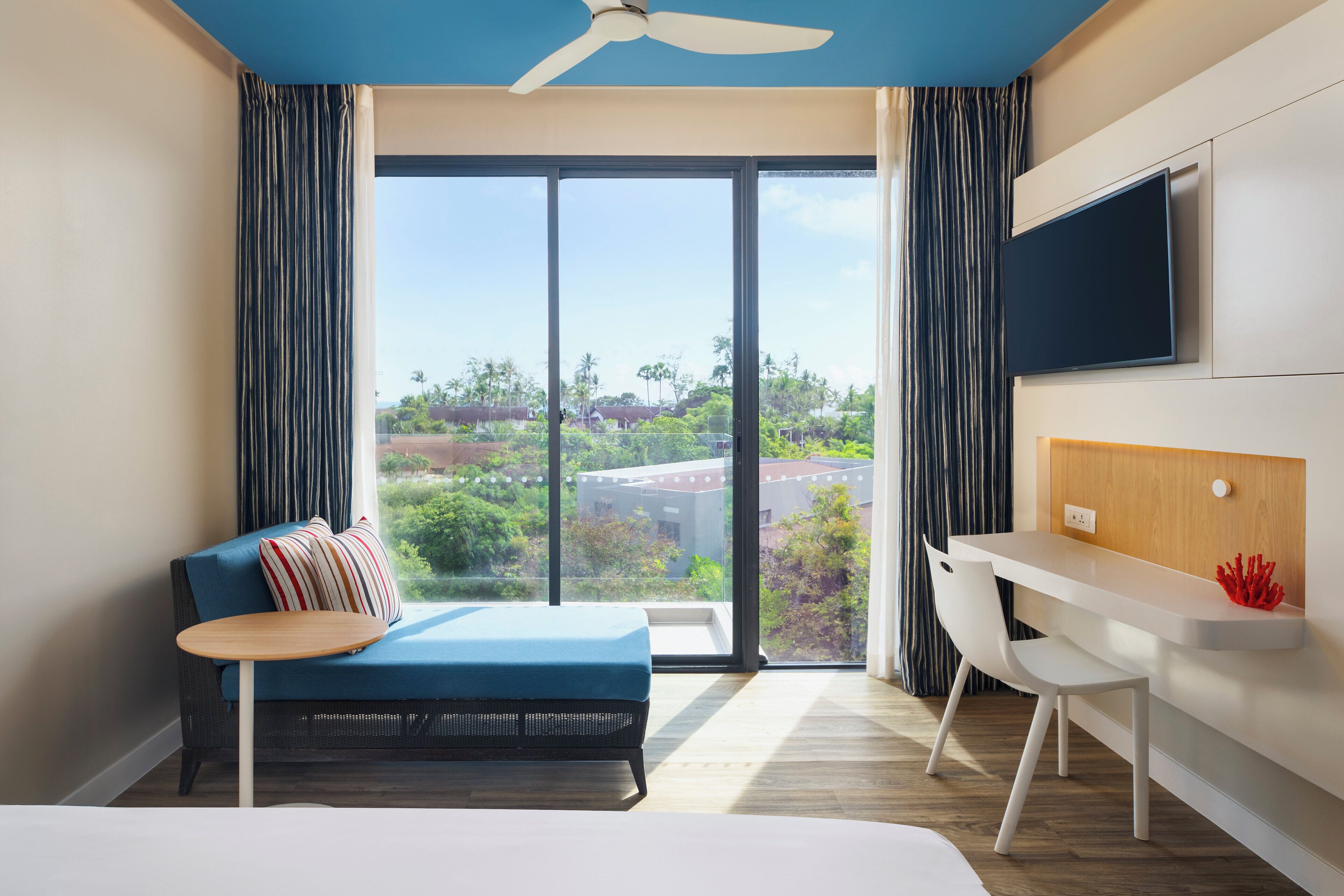 Une chambre d’hôtel moderne dotée d’une grande fenêtre, d’un canapé, d’un bureau et d’un téléviseur à écran plat.