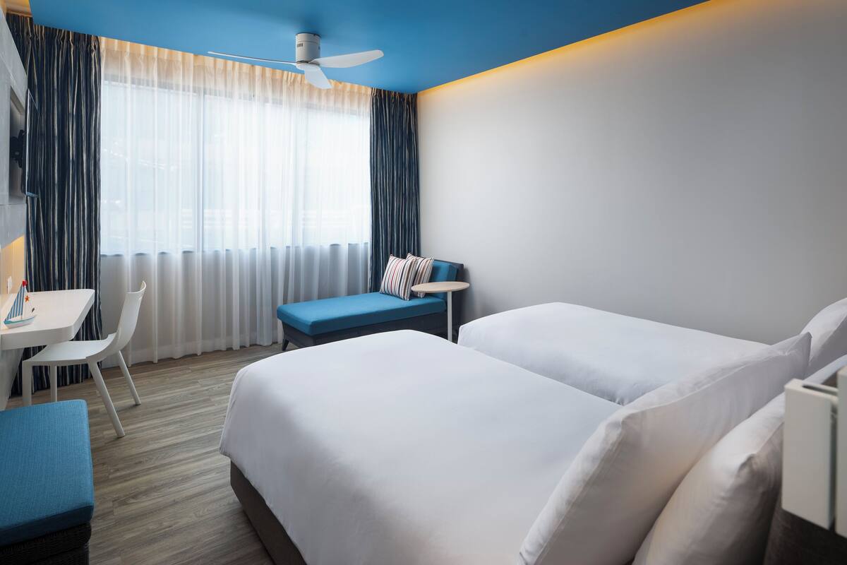 A hotel room with two beds, a desk, a chair, and a small table.