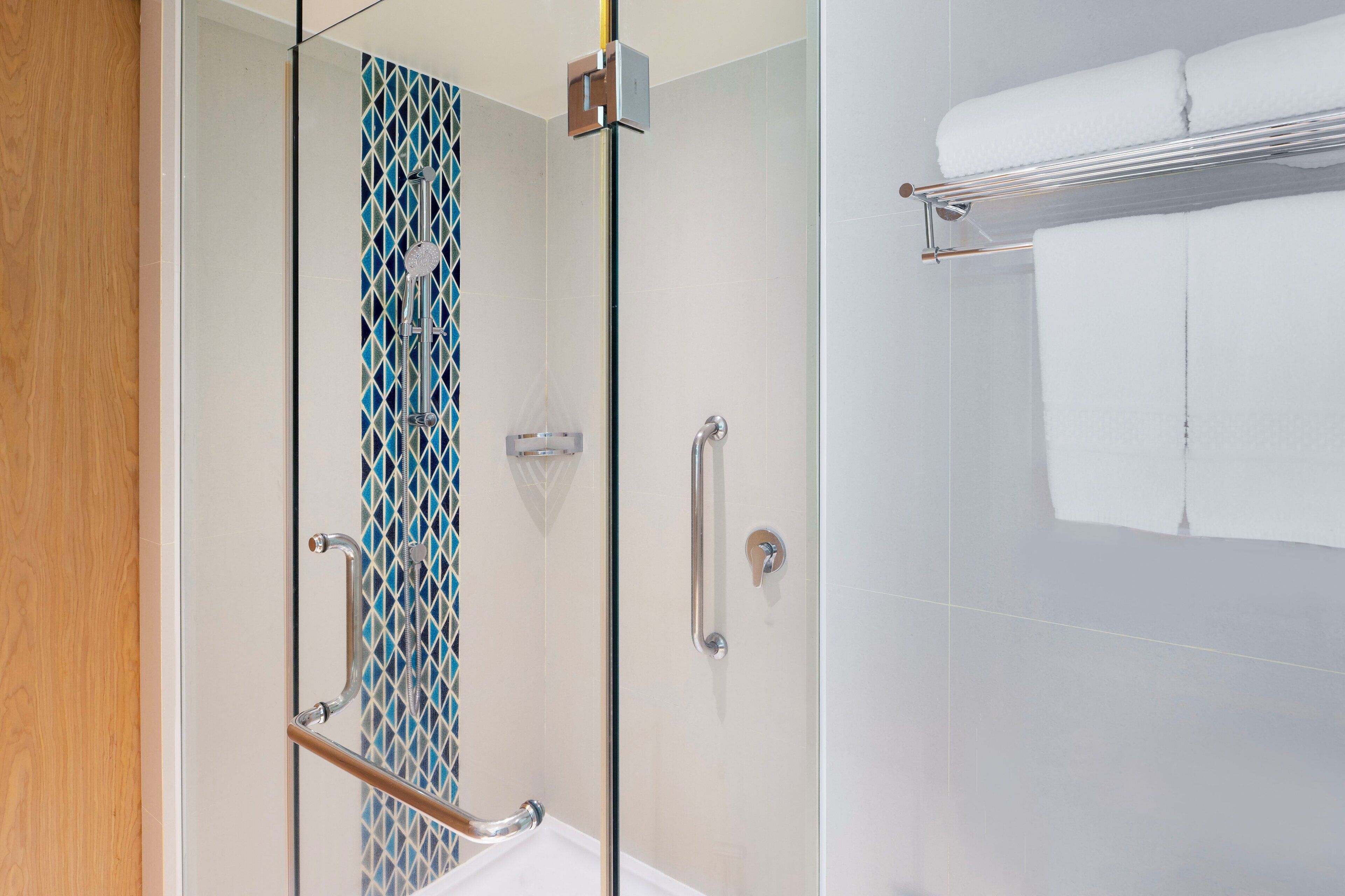 A modern bathroom with a glass shower enclosure, a towel rack, and a patterned tile backsplash.