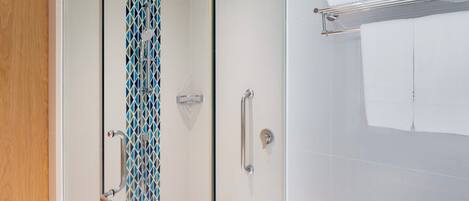A modern bathroom with a glass shower enclosure, a towel rack, and a patterned tile backsplash.