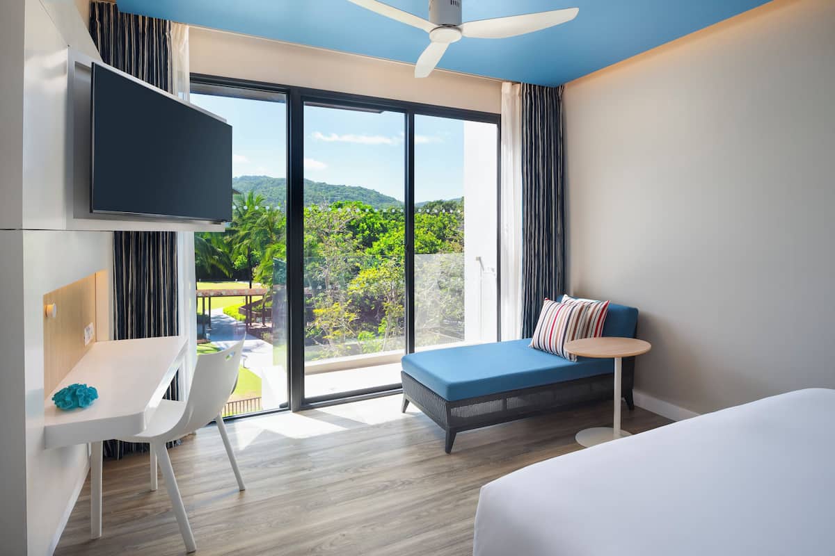 A modern hotel room with a large window, a bed, a desk, and a TV.