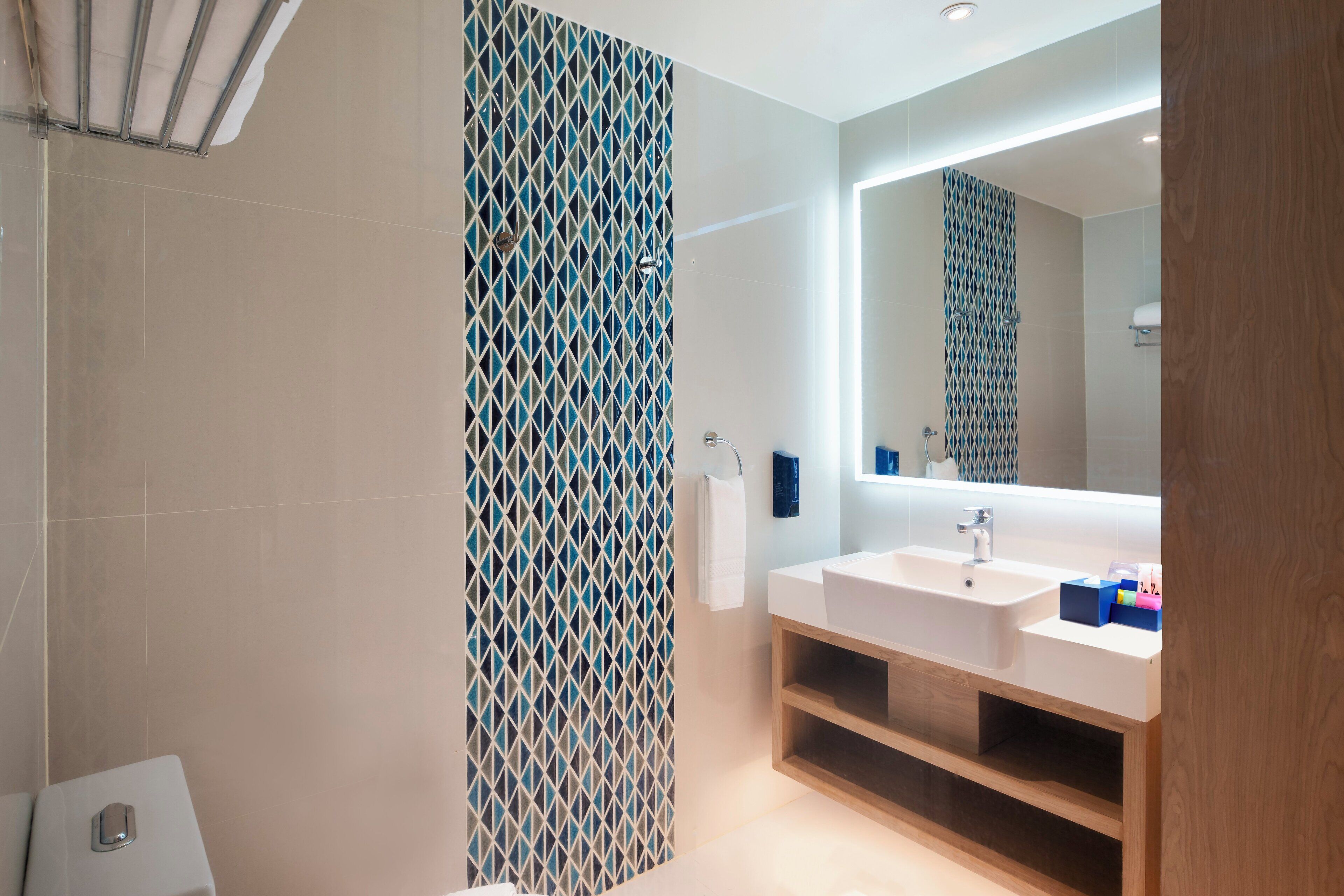 Un baño moderno con un espejo grande, un lavamanos blanco y una cortina de ducha estampada.