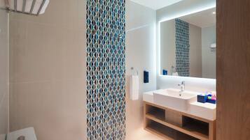 Un baño moderno con un espejo grande, un lavamanos blanco y una cortina de ducha estampada.