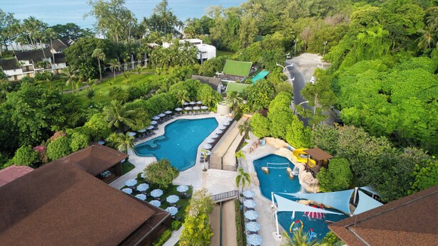 Um resort com uma piscina grande, várias áreas de lounge com guarda-sóis e vista para o oceano e uma ilha pequena.