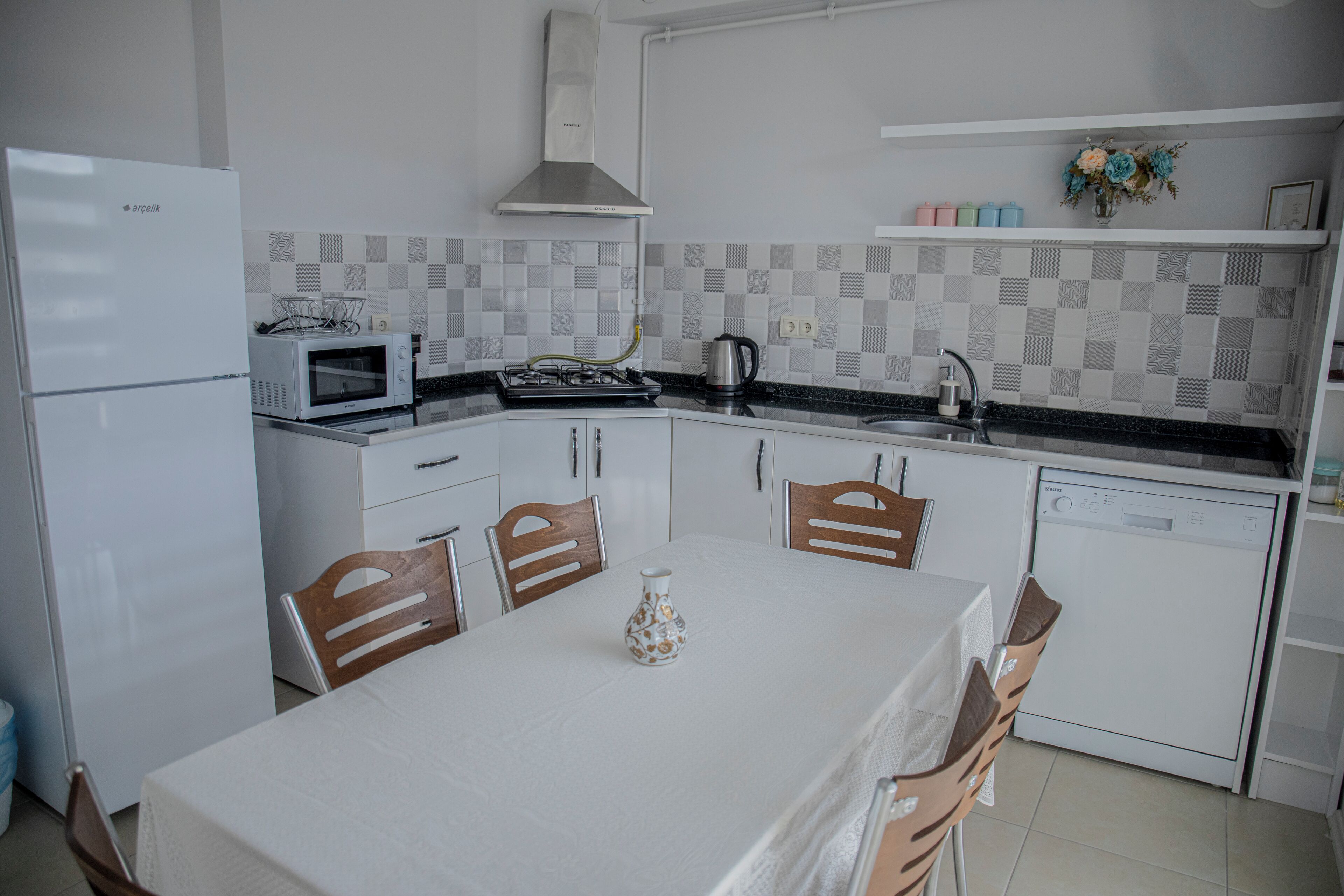 A modern kitchen with white appliances, a tiled backsplash, and a dining area with a table and chairs.