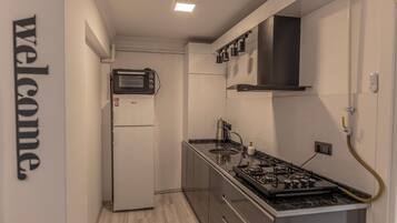 Cocina compacta con microondas, refrigerador, estufa y un letrero que dice 'bienvenido' en la pared.