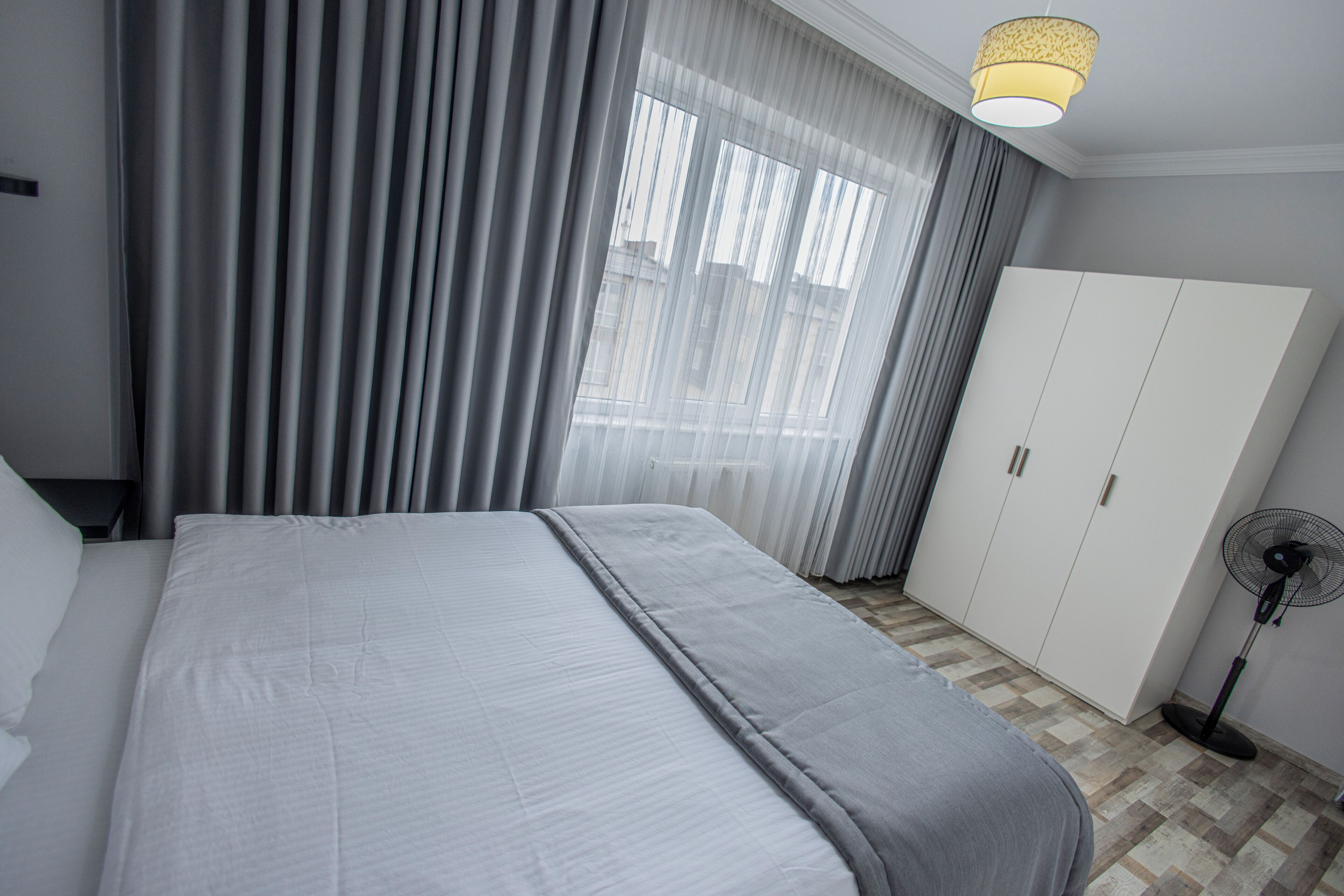 A bedroom with a bed, a wardrobe, a fan, and a window with curtains.