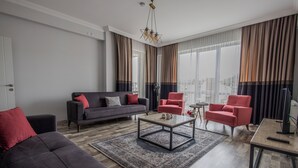 Ein modernes Wohnzimmer mit einem grauen Sofa, roten Sessel, einem Couchtisch und Blick auf die Stadt durch große Fenster.