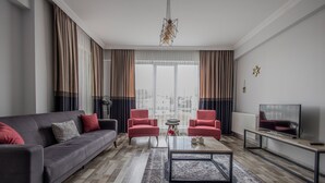 Ein modernes Wohnzimmer mit einer grauen Couch, zwei roten Sesseln, einem Couchtisch und einem Fernseher auf einem Schrank.