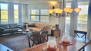 Un salón amplio con mesa de comedor de madera, asientos cómodos y ventanas grandes.