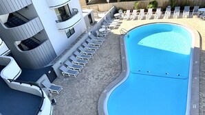 Una piscina con sillones de descanso y un edificio con varios balcones.