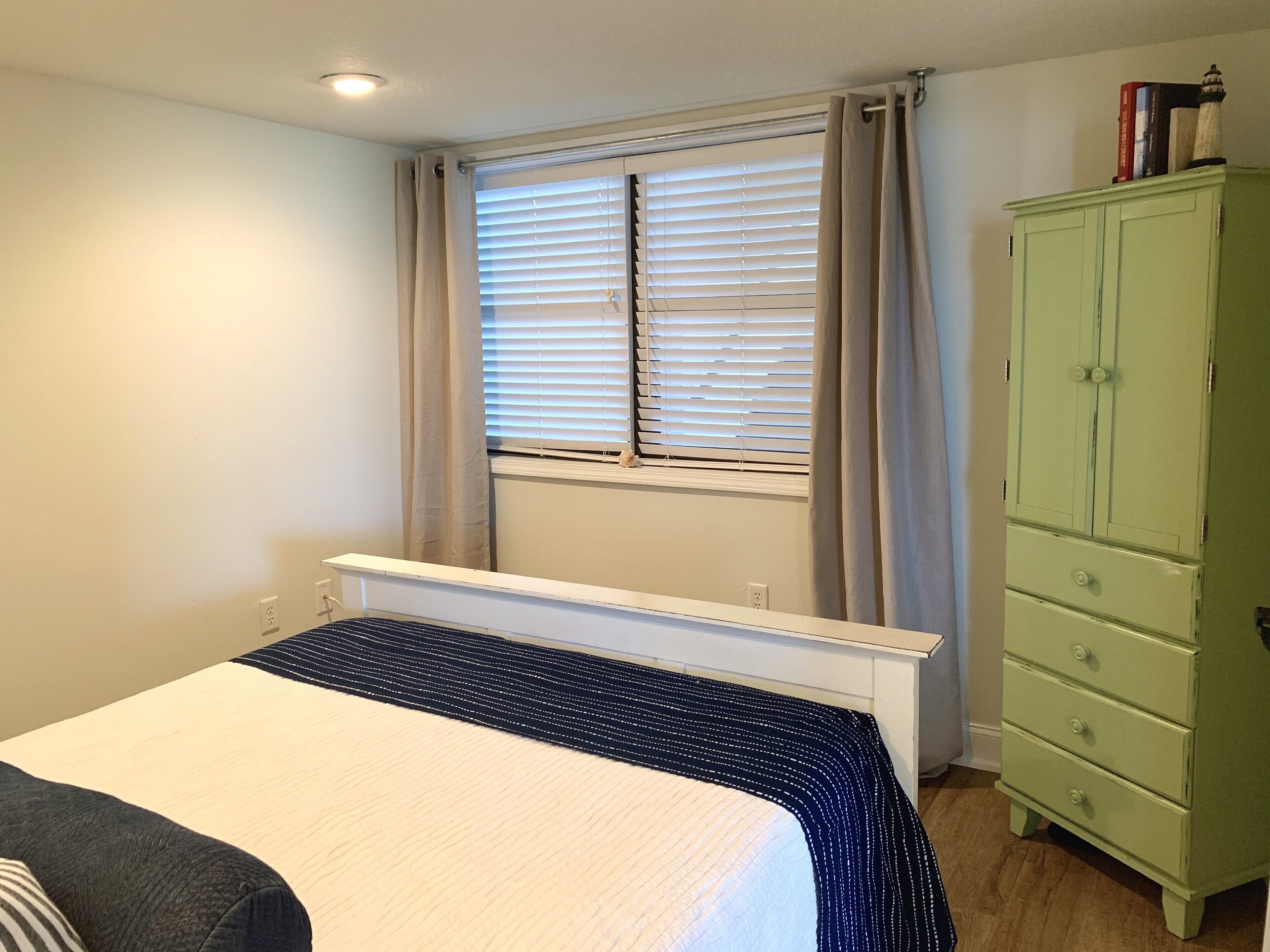 Un dormitorio con cama, ventana con persianas, radiador y cómoda verde.
