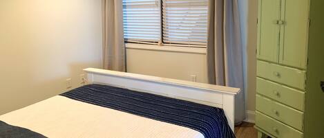 Un dormitorio con cama, ventana con persianas, radiador y cómoda verde.