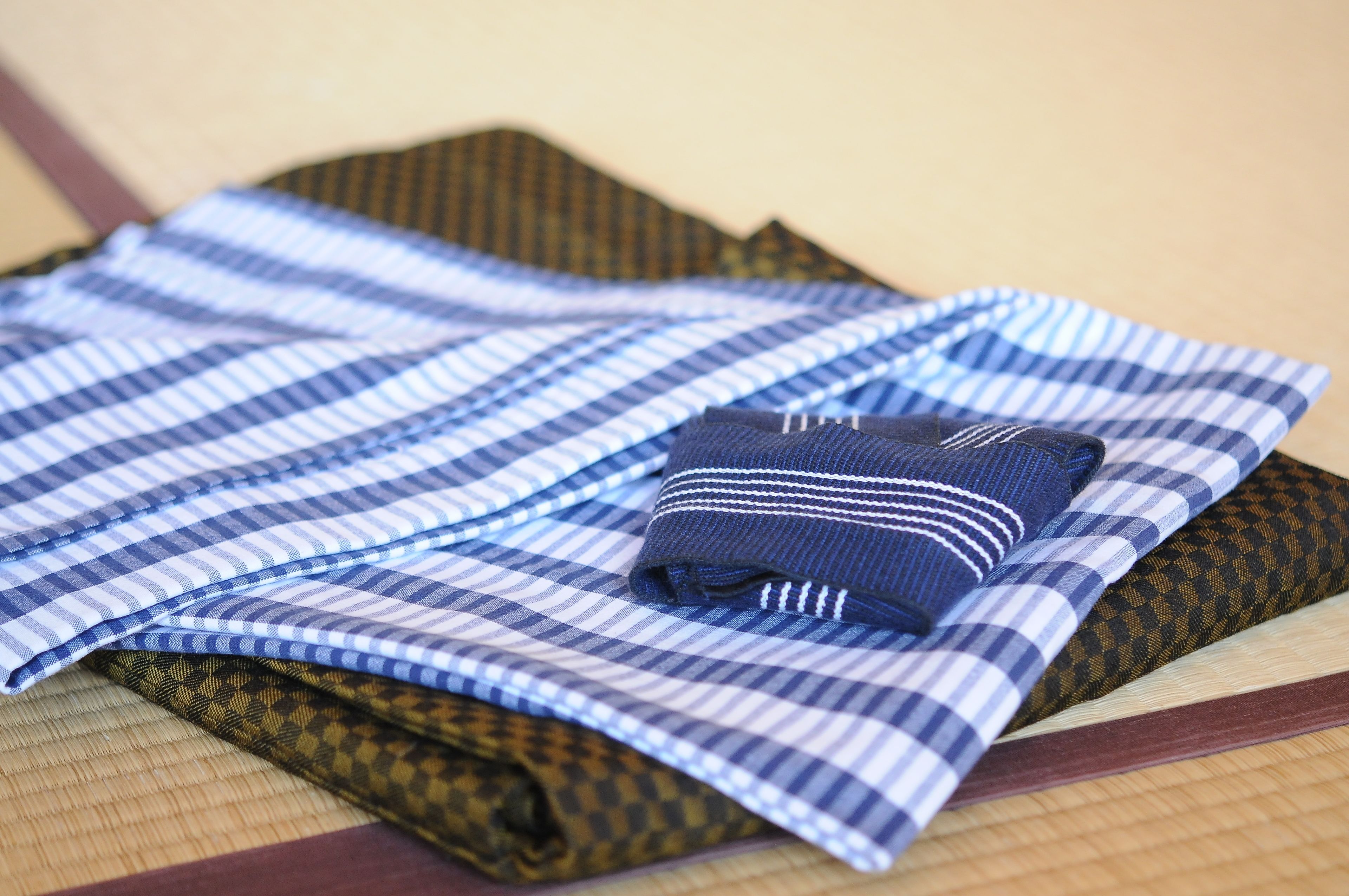 A neatly folded set of checkered tablecloths in various patterns and colors, including blue, brown, and black, arranged on a wooden surface.