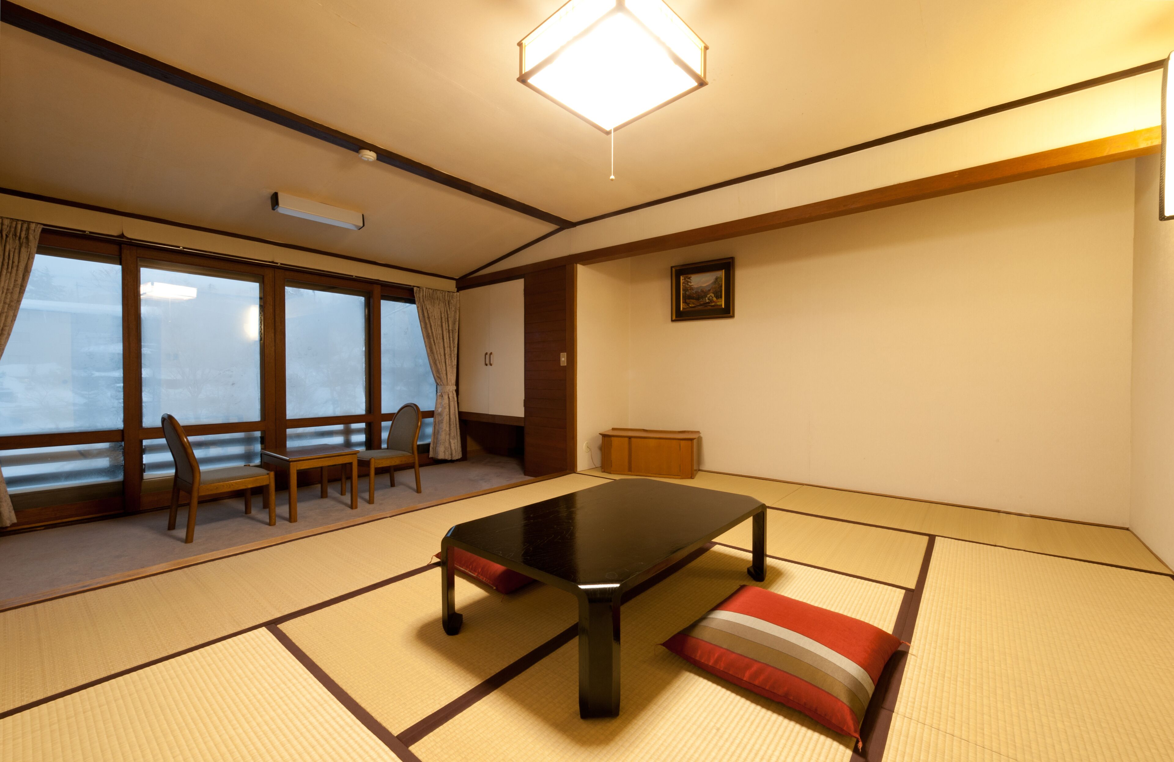 Een traditionele Japanse kamer met tatami vloerbedekking, een lage tafel en uitzicht door grote ramen.