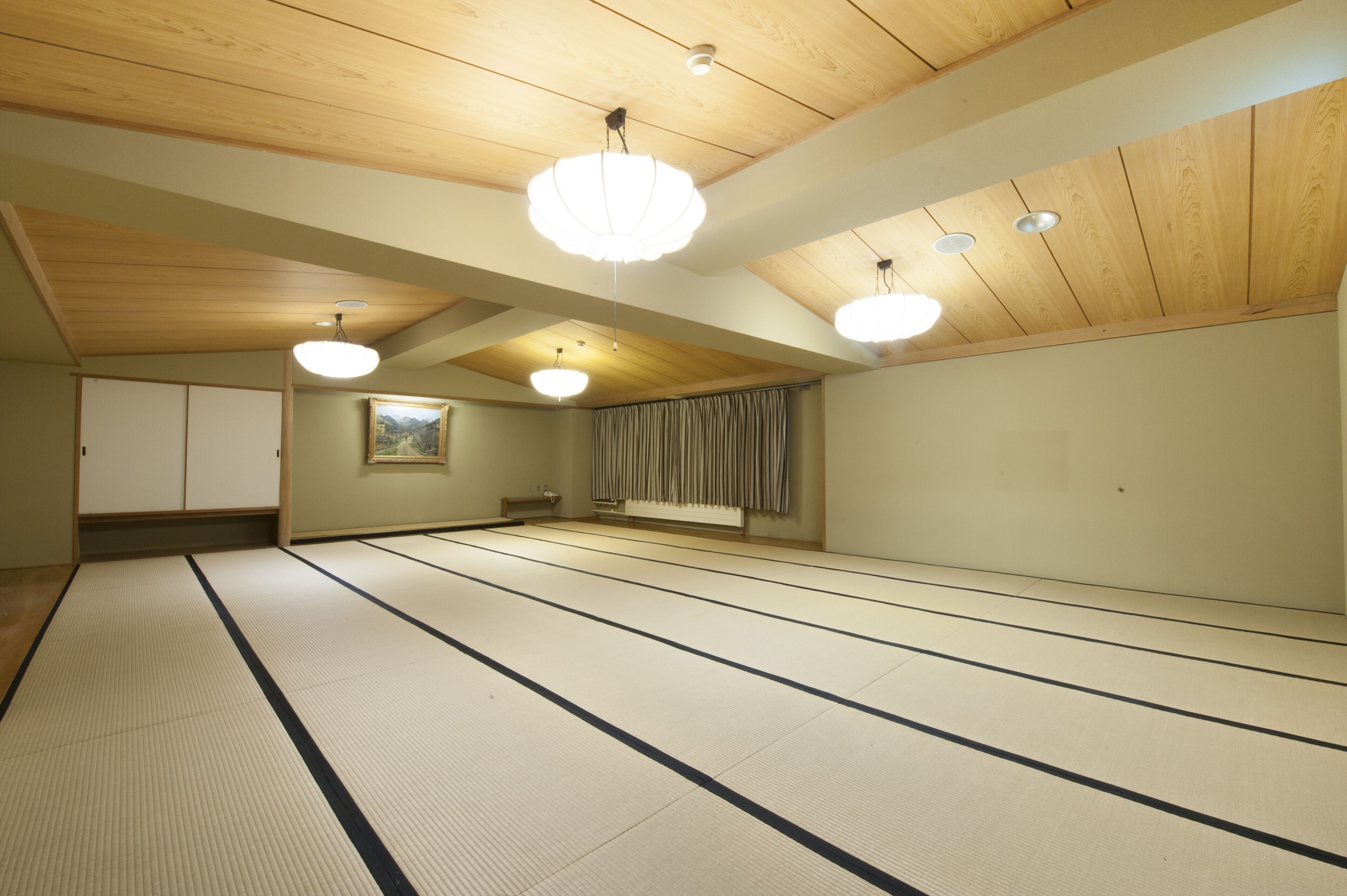 A tatami mat room with wooden beams, tatami mats, a painting, and a sliding door.