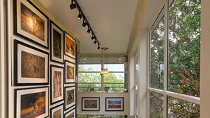 A hallway with framed wildlife photographs on the walls, a staircase leading to a balcony with potted plants, and large windows offering a view of greenery outside. - Haze and Kites Resort Munnar (Devikolam)