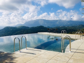 An infinity pool with clear water, metal railings, and a view of mountains and hills in the background. - Haze and Kites Resort Munnar (Devikolam)