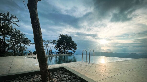 A serene pool area with a clear view of the sea and mountains, surrounded by trees and a stone pathway. - Haze and Kites Resort Munnar (Devikolam)