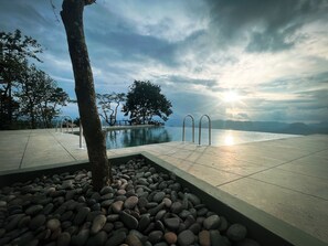 Un área de piscina tranquila con vistas despejadas al mar y a las montañas, rodeada de árboles y un sendero de piedra.