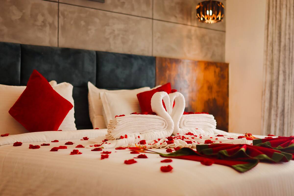 A neatly made bed with white linens, red pillows, and a decorative swan made of towels.