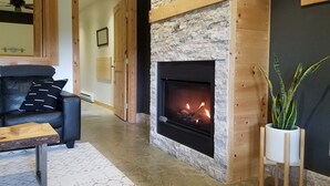 Een woonkamer met een stenen openhaard, een zwarte leren bank en een houten salontafel.