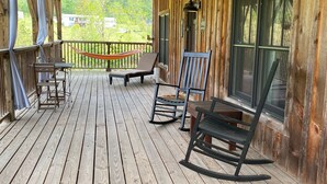 Een houten terras met een tafel, stoelen, een hangmat en een schommelstoel.