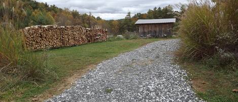 A gravel path leading to a rustic wooden building with a metal roof, surrounded by a natural landscape with trees and grass.