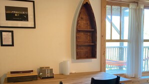 Een kamer met een houten bureau, twee zwarte stoelen, een lijst met een afbeelding en een houten plank.